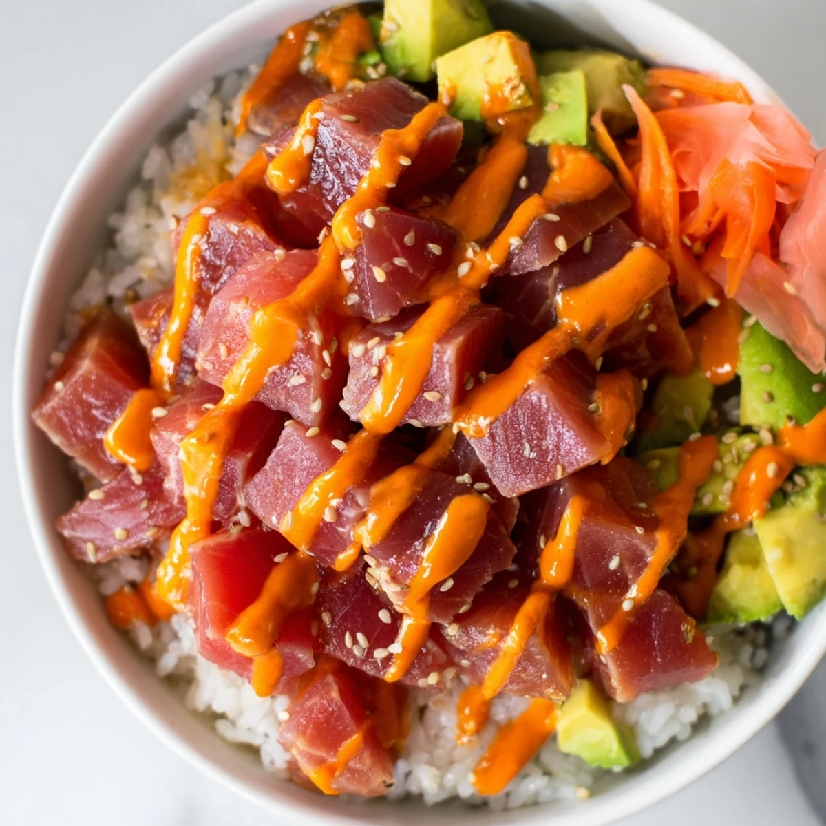 A vibrant Spicy Tuna Poke Bowl topped with creamy sriracha mayo, sliced avocado, and crunchy nori strips over a bed of seasoned rice.