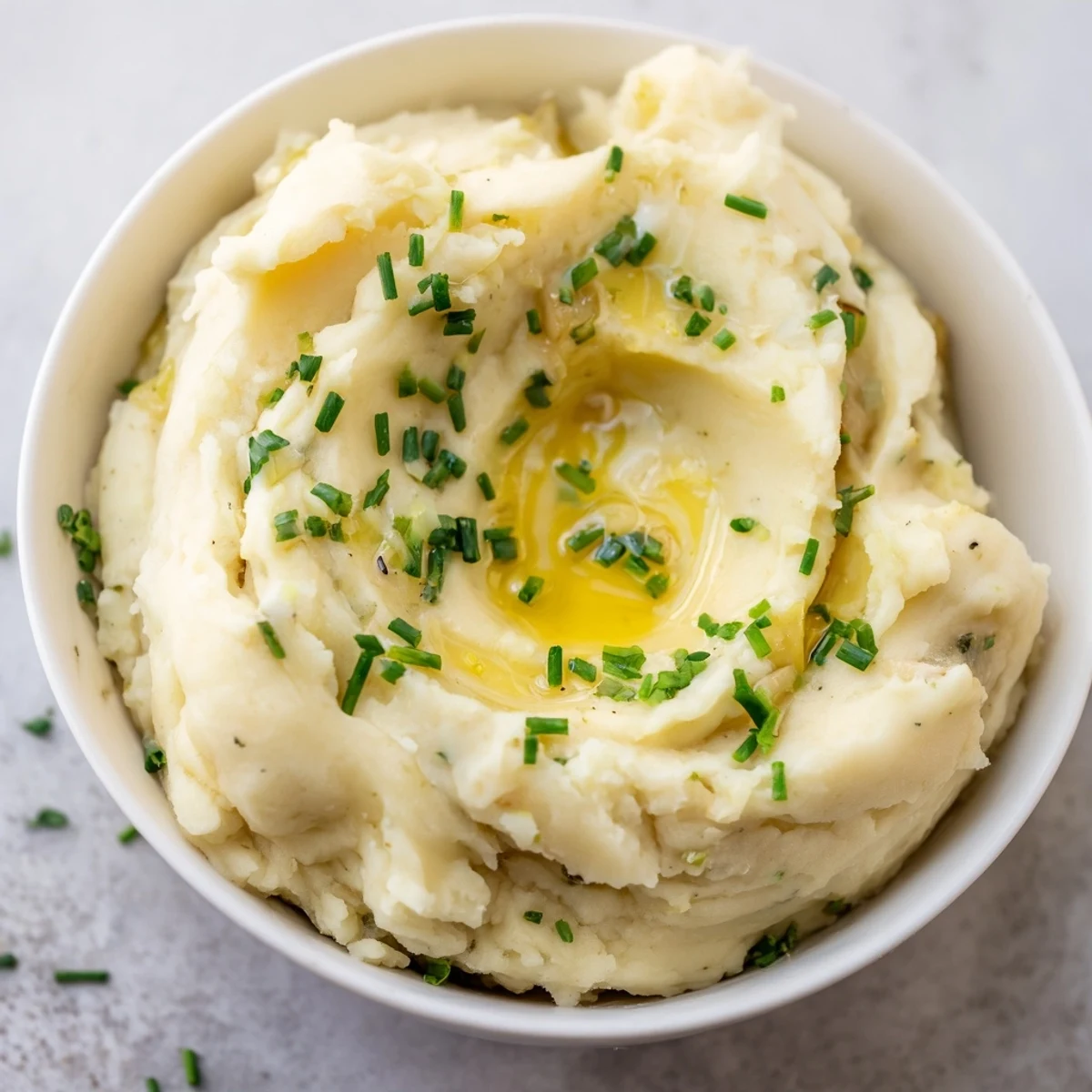 Golden Yukon Gold Roasted Garlic Mashed Potatoes served hot in a ceramic bowl, garnished with fresh herbs for a comforting side dish.