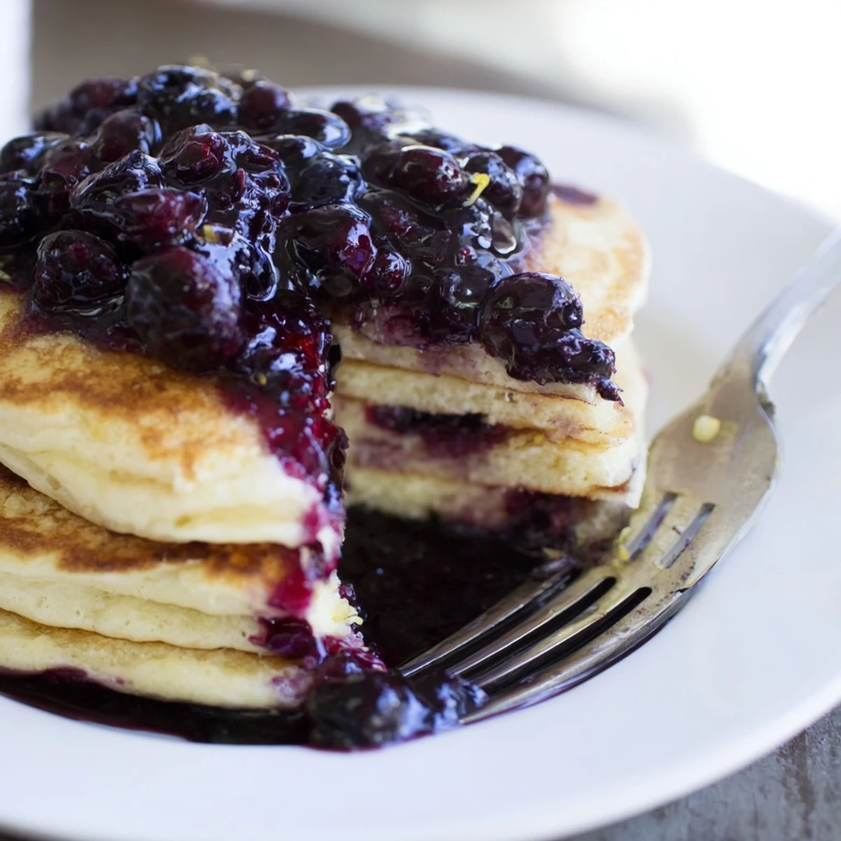 Golden-brown, fluffy Lemon Ricotta Pancakes stacked high and drizzled generously with deep purple, warm blueberry syrup.