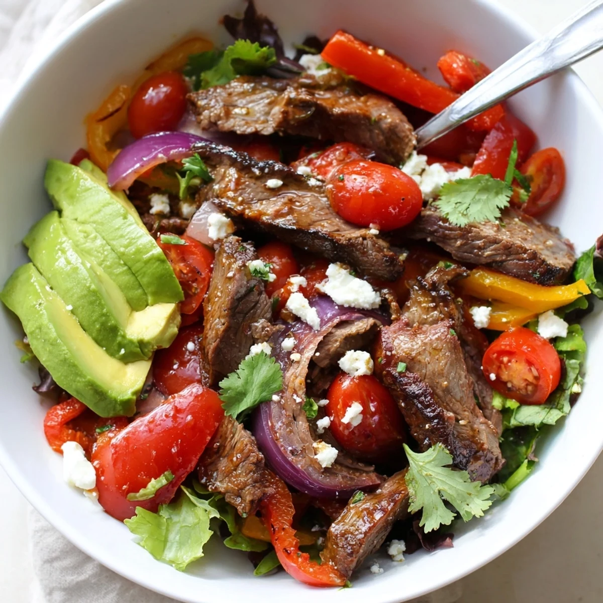 Fresh lime vinaigrette dressed Beef Fajita Salad with creamy avocado slices and crumbled cotija cheese ready to serve.