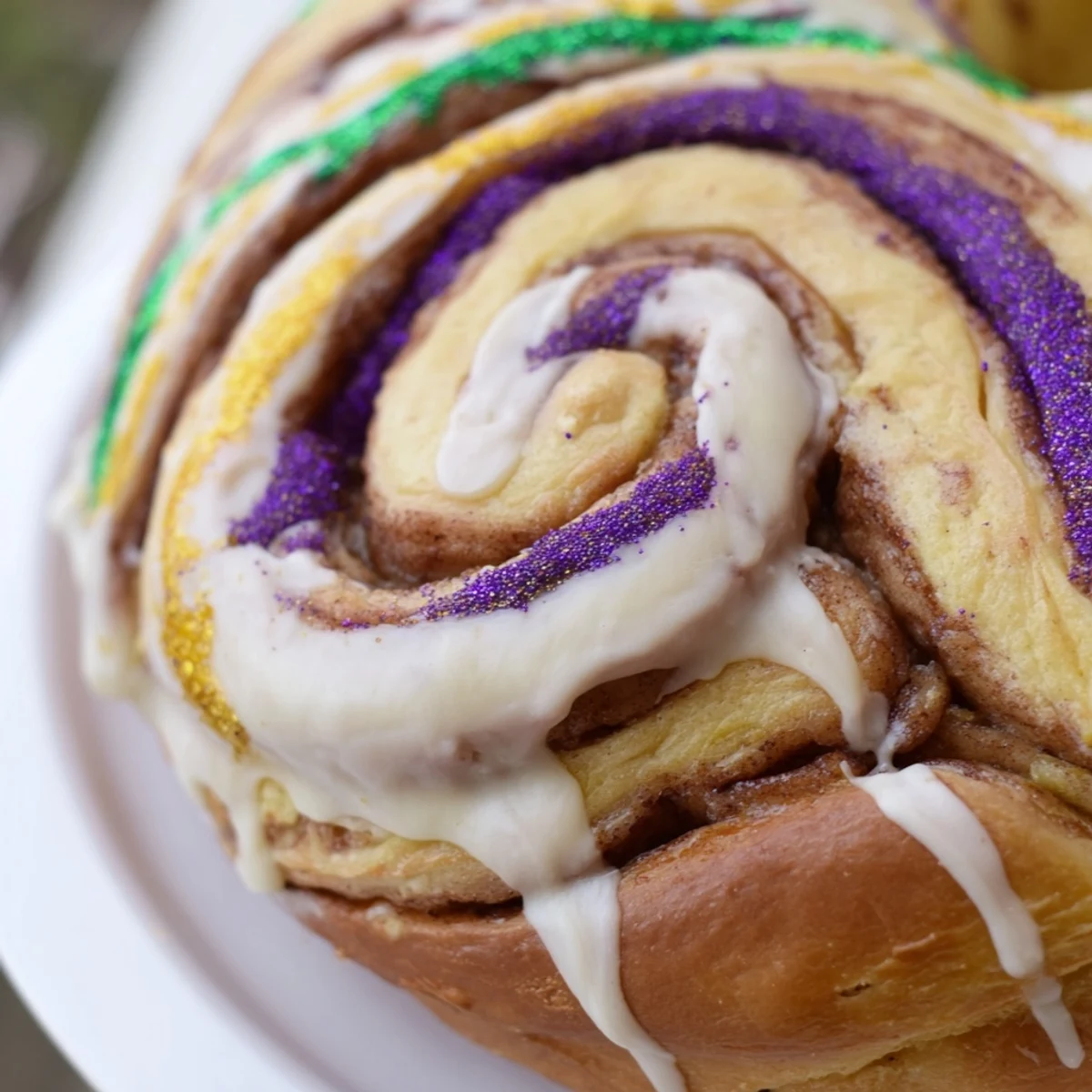 A festive slice of King Cake showing layers of cinnamon swirl and colorful Mardi Gras sugars.  