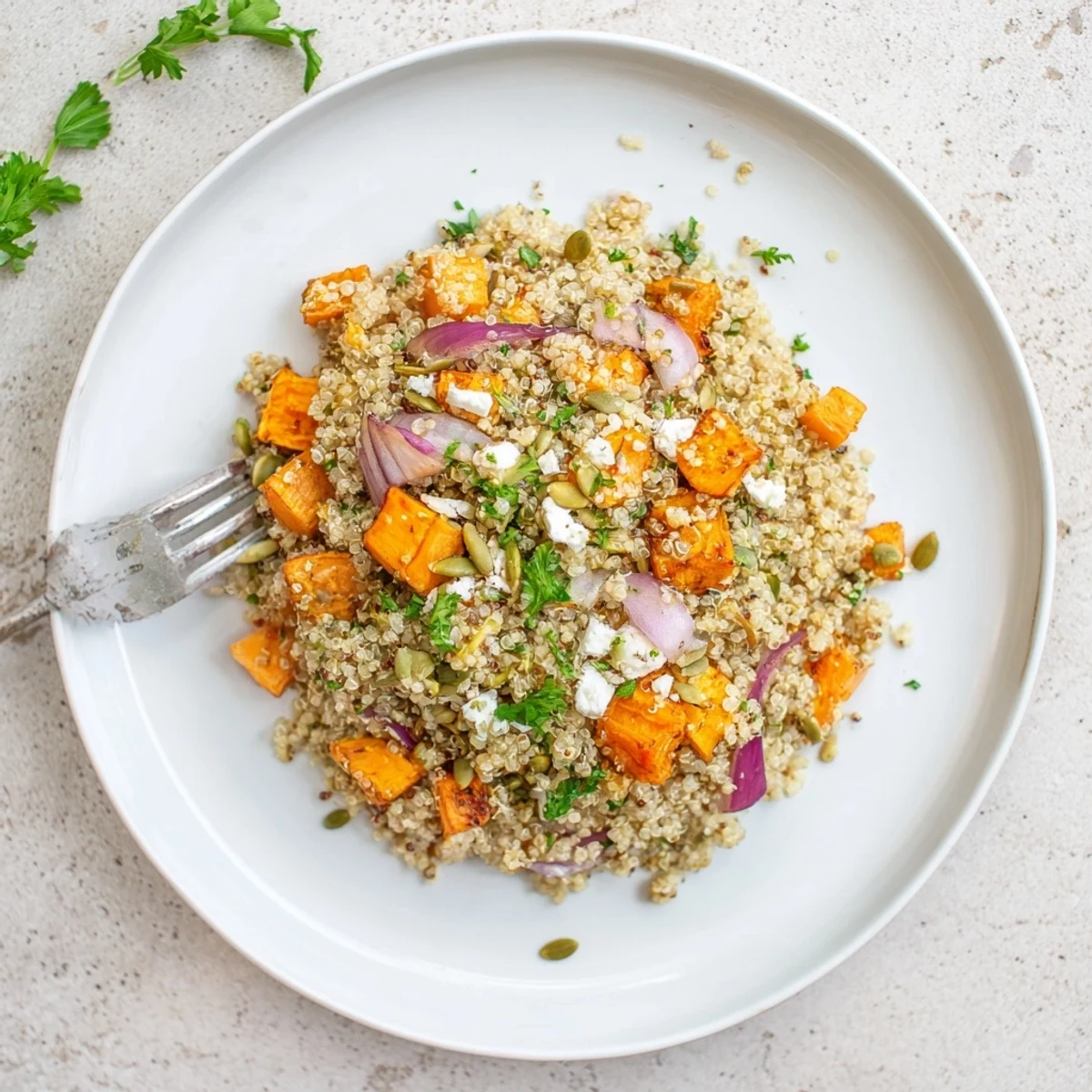 A vibrant bowl of Warm Quinoa Salad with Roasted Root Vegetables, topped with parsley, feta, and crunchy pumpkin seeds.