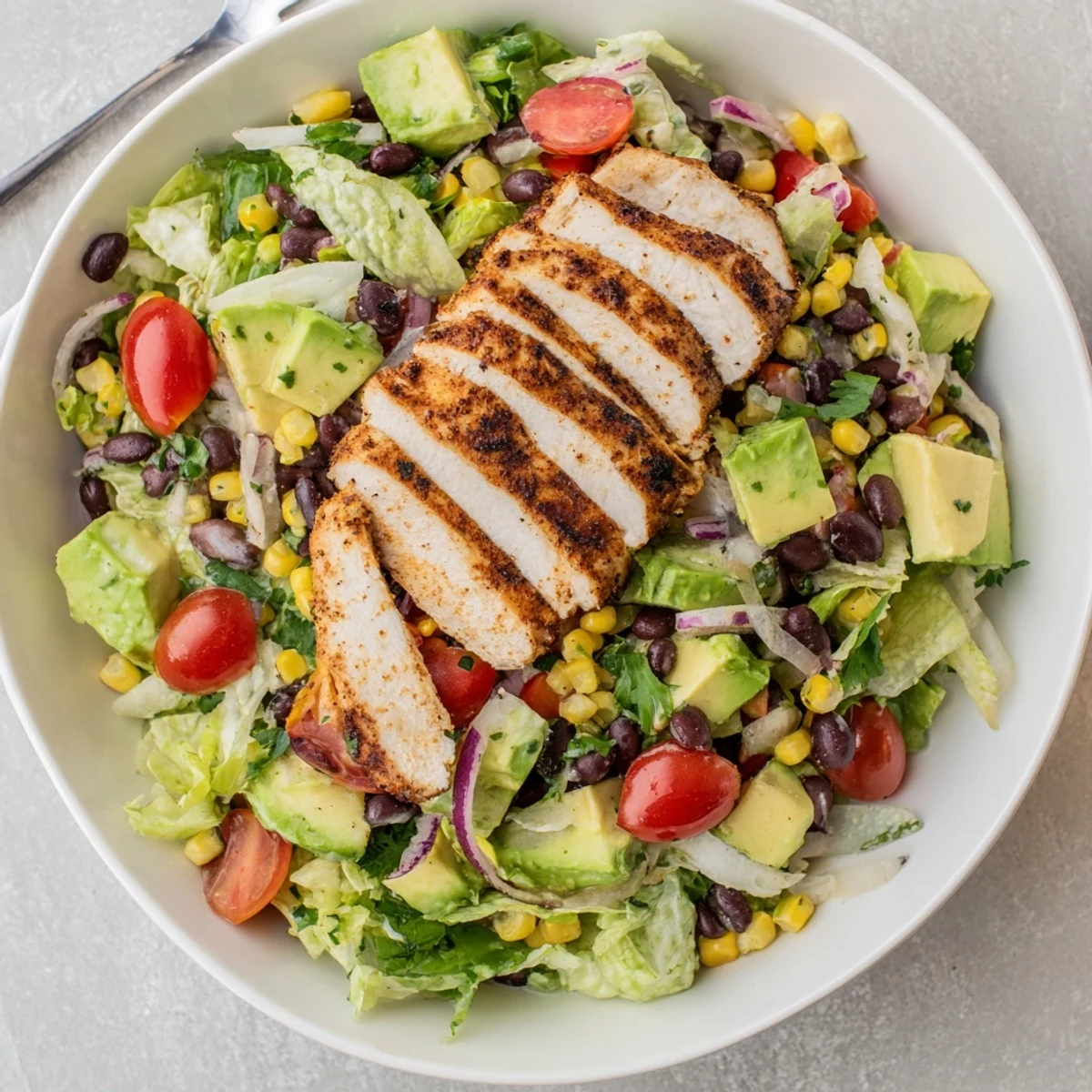 Grilled chicken slices top a vibrant Southwest Chicken Salad with black beans, corn, and avocado in a zesty lime dressing.