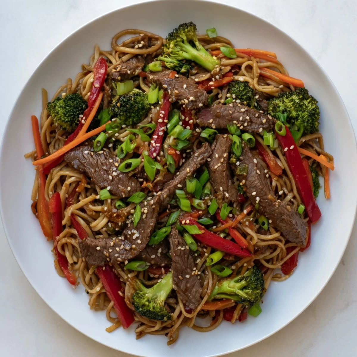 Steaming Beef and Broccoli Lo Mein served in a bowl, garnished with green onions and toasted sesame seeds.