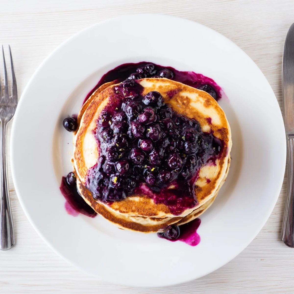 A close-up of golden Lemon Ricotta Pancakes with Blueberry Syrup, featuring a dollop of whipped cream and lemon zest.  