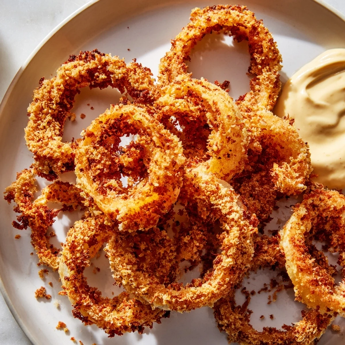 Crispy air fryer onion rings arranged with creamy dipping sauce, golden brown and perfectly crunchy on the edges.  