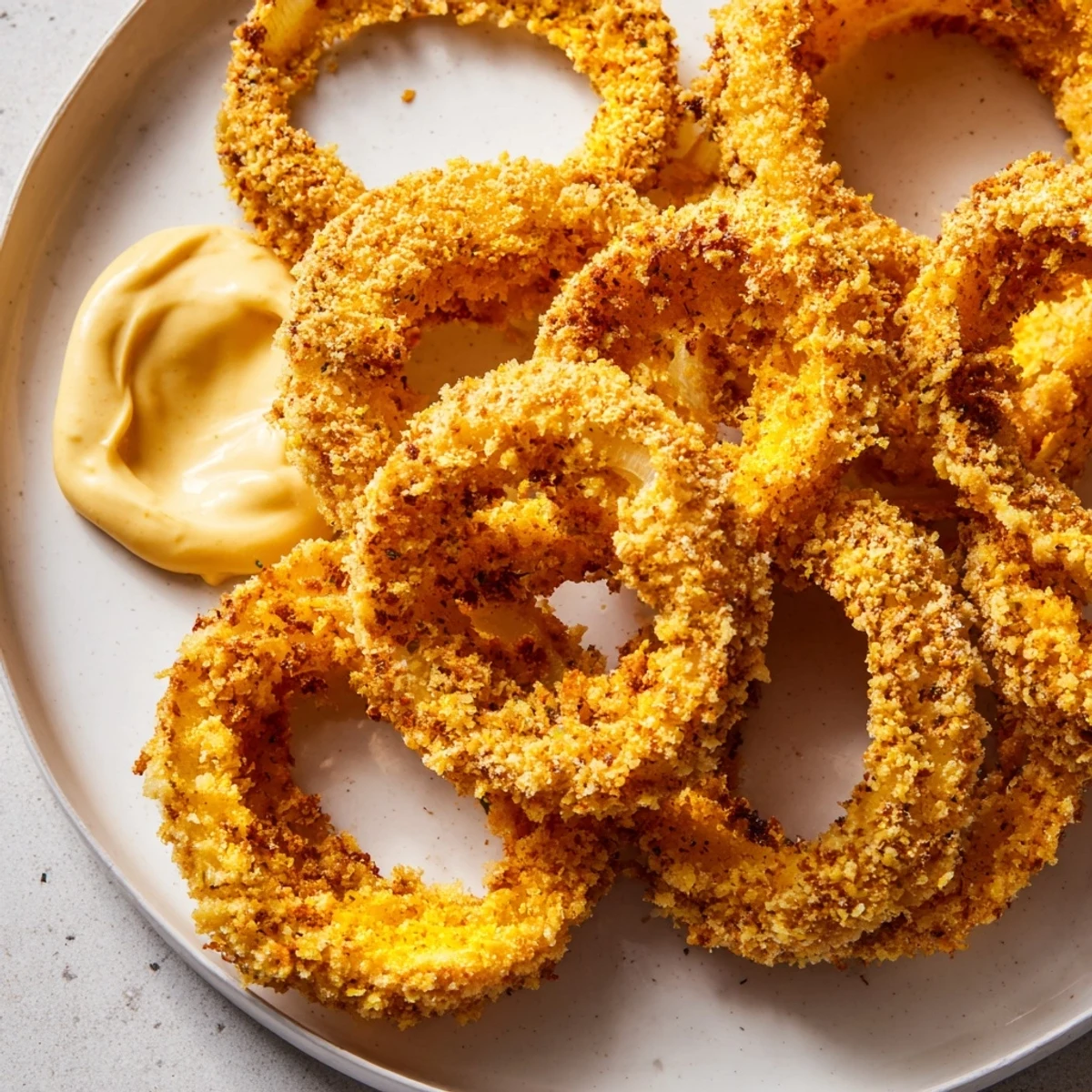 Hearty platter of air fryer onion rings featuring golden breadcrumbs and a tangy dip for an appetizer snack.  