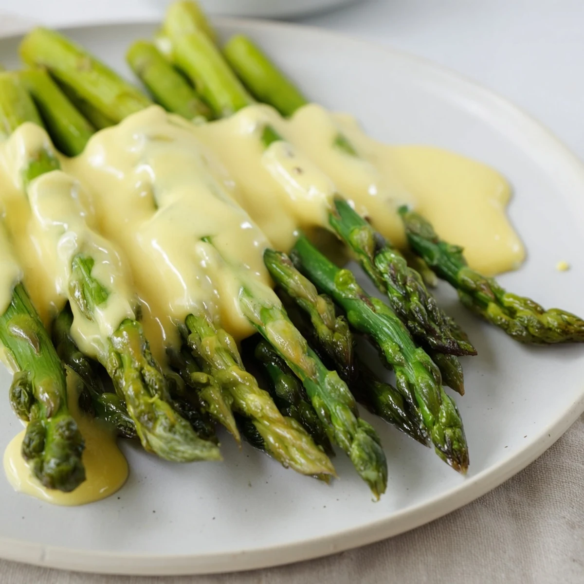 Golden-brown roasted asparagus with Hollandaise sauce served on a white platter.