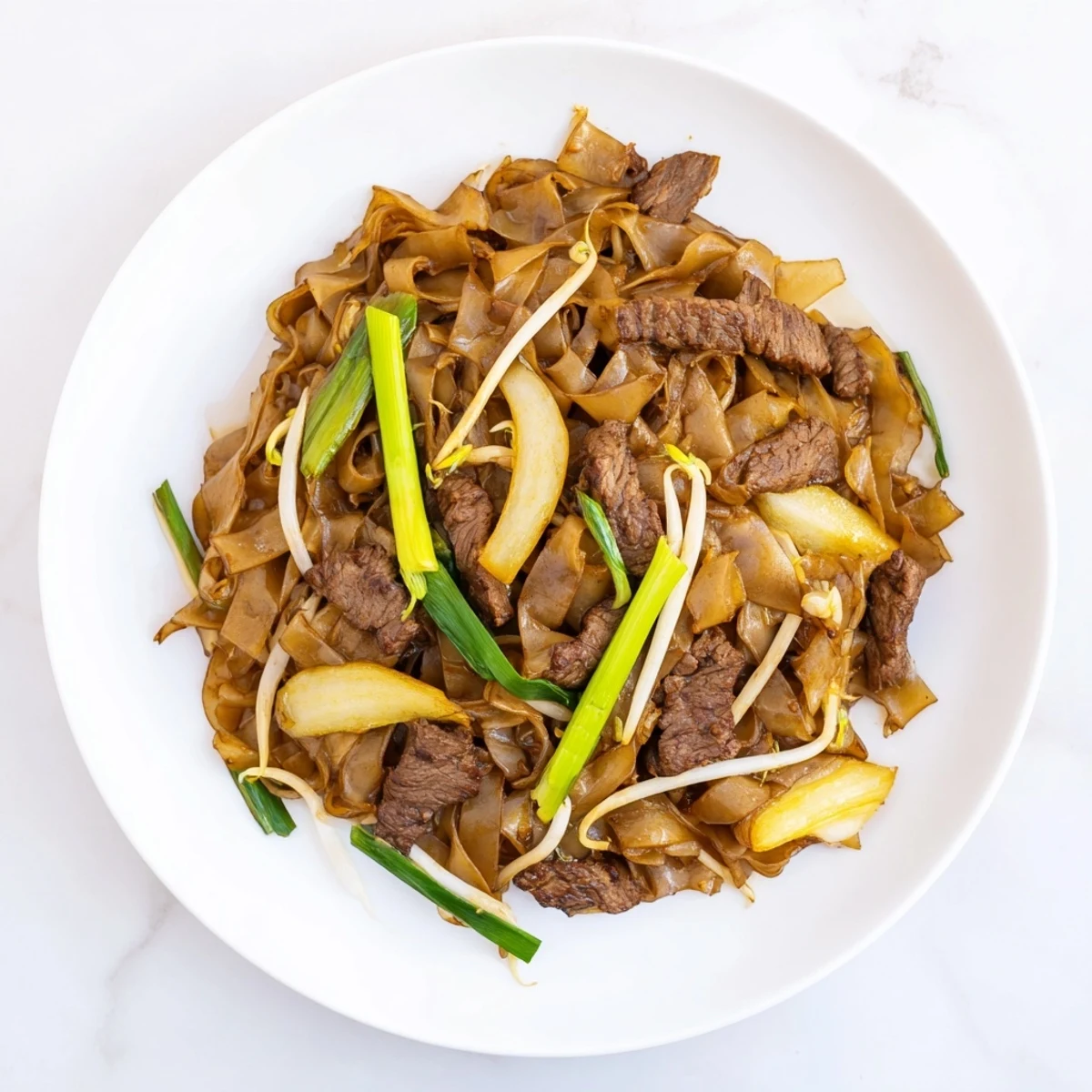 A close-up of Beef Chow Fun with wide noodles, seared beef, and fresh bean sprouts in a savory sauce.