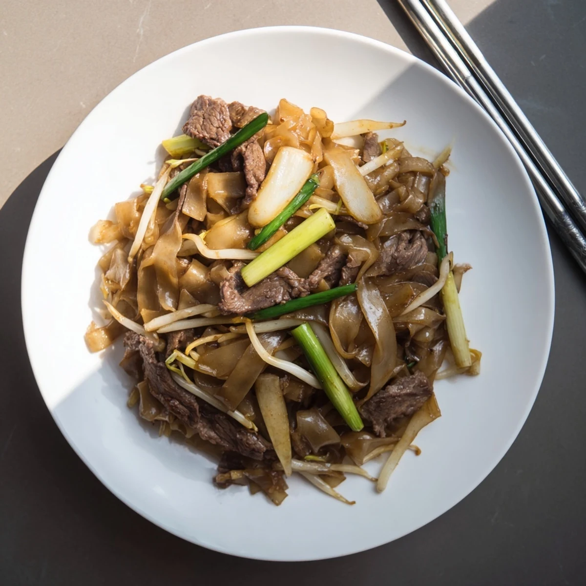 Steaming hot Beef Chow Fun in a bowl, garnished with spring onions for a classic Cantonese stir-fry presentation.