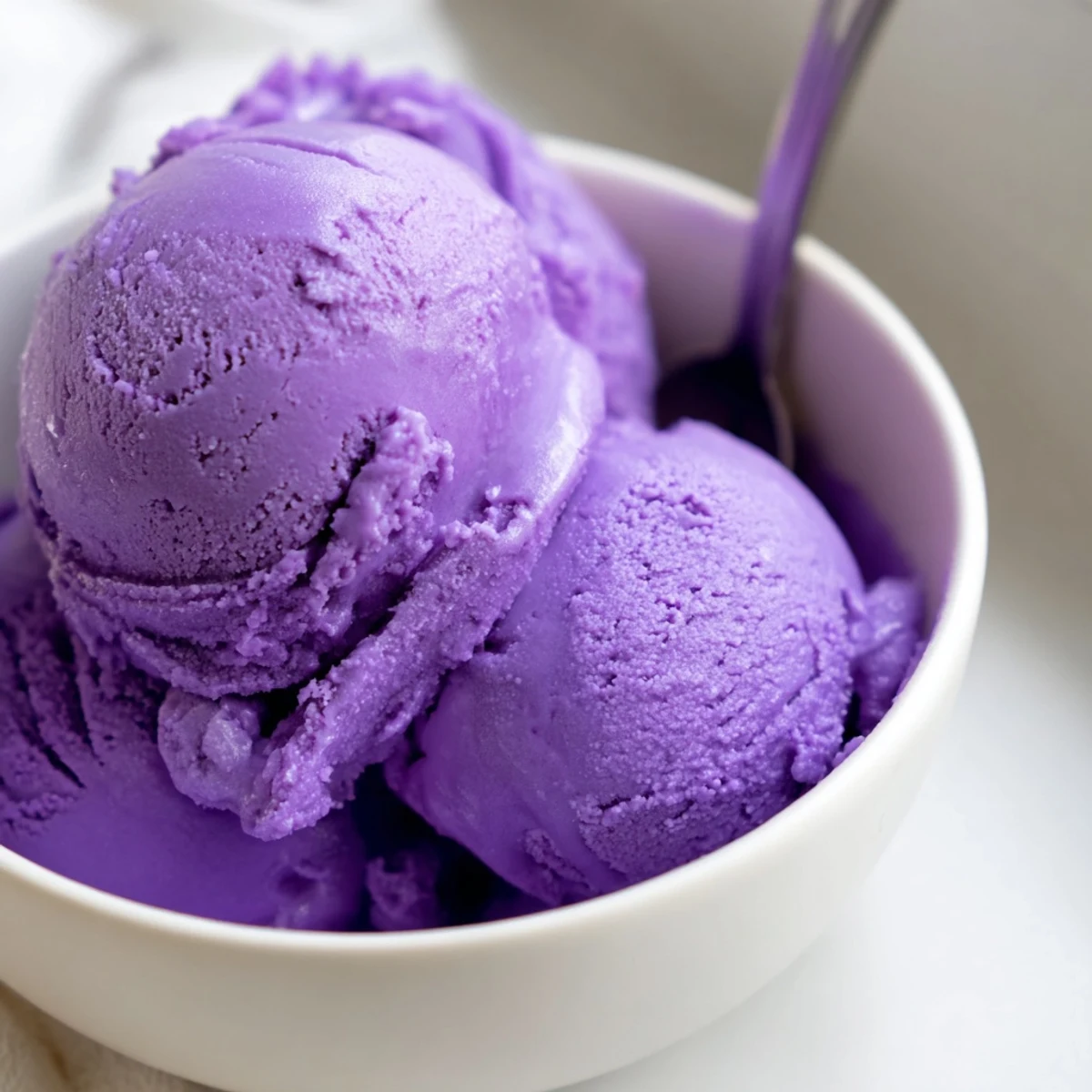 A scoop of vibrant Ube Ice Cream is served in a white bowl with a wooden spoon.