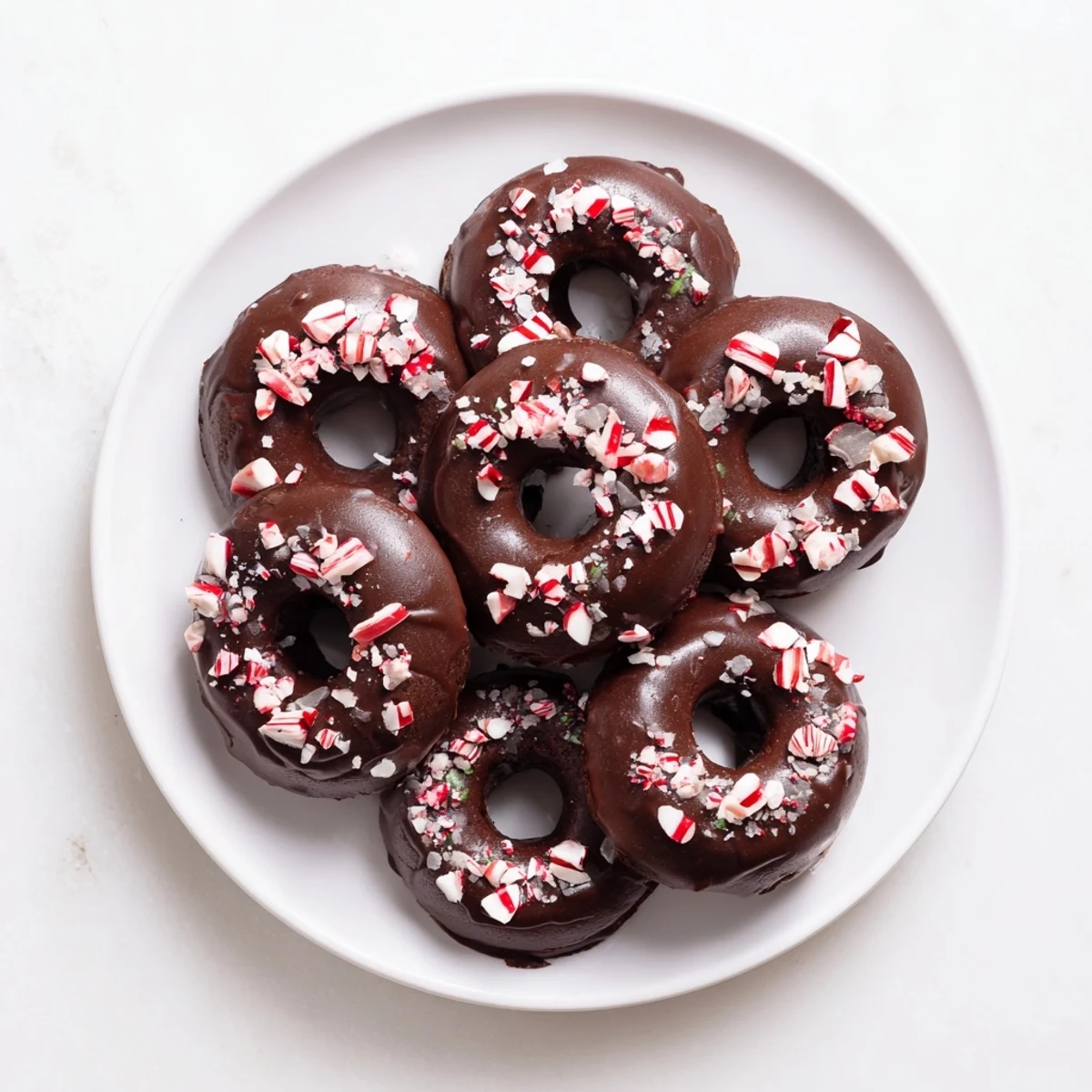 Freshly baked Chocolate Peppermint Mochi Donuts with a glossy chocolate glaze and crushed candy cane pieces on a wire rack.