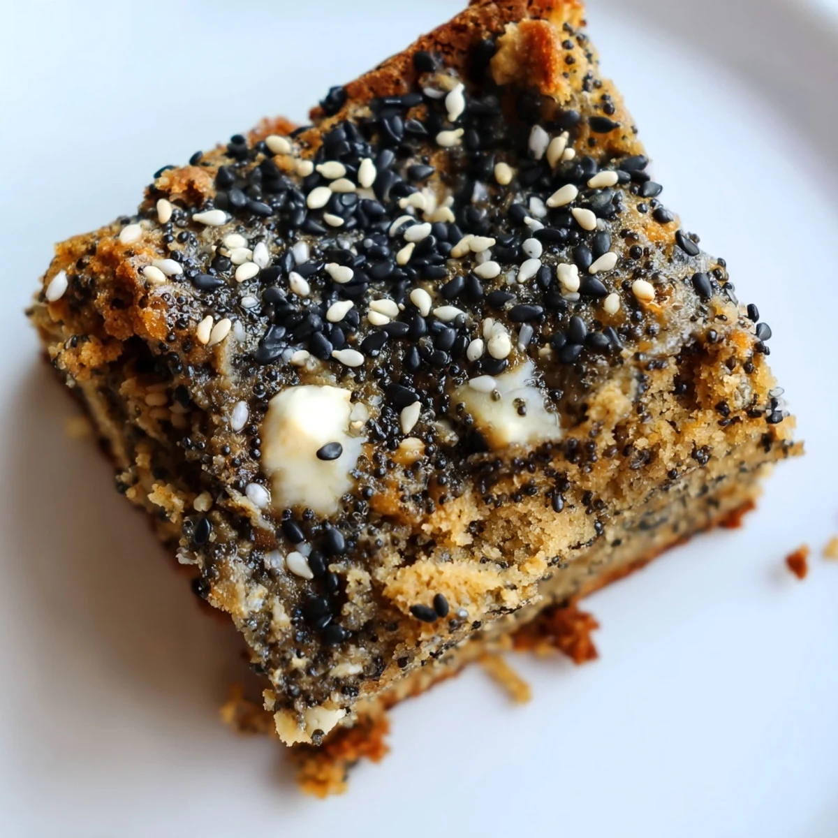 Golden squares of Black Sesame Blondies sit atop a wooden cutting board, topped with whole black sesame seeds and a drizzle of melted white chocolate.
