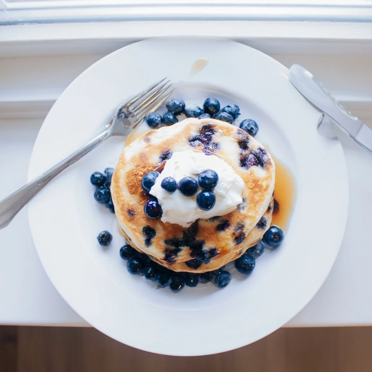 Stack of Greek Yogurt Blueberry Pancakes topped with fresh blueberries and a drizzle of maple syrup.  