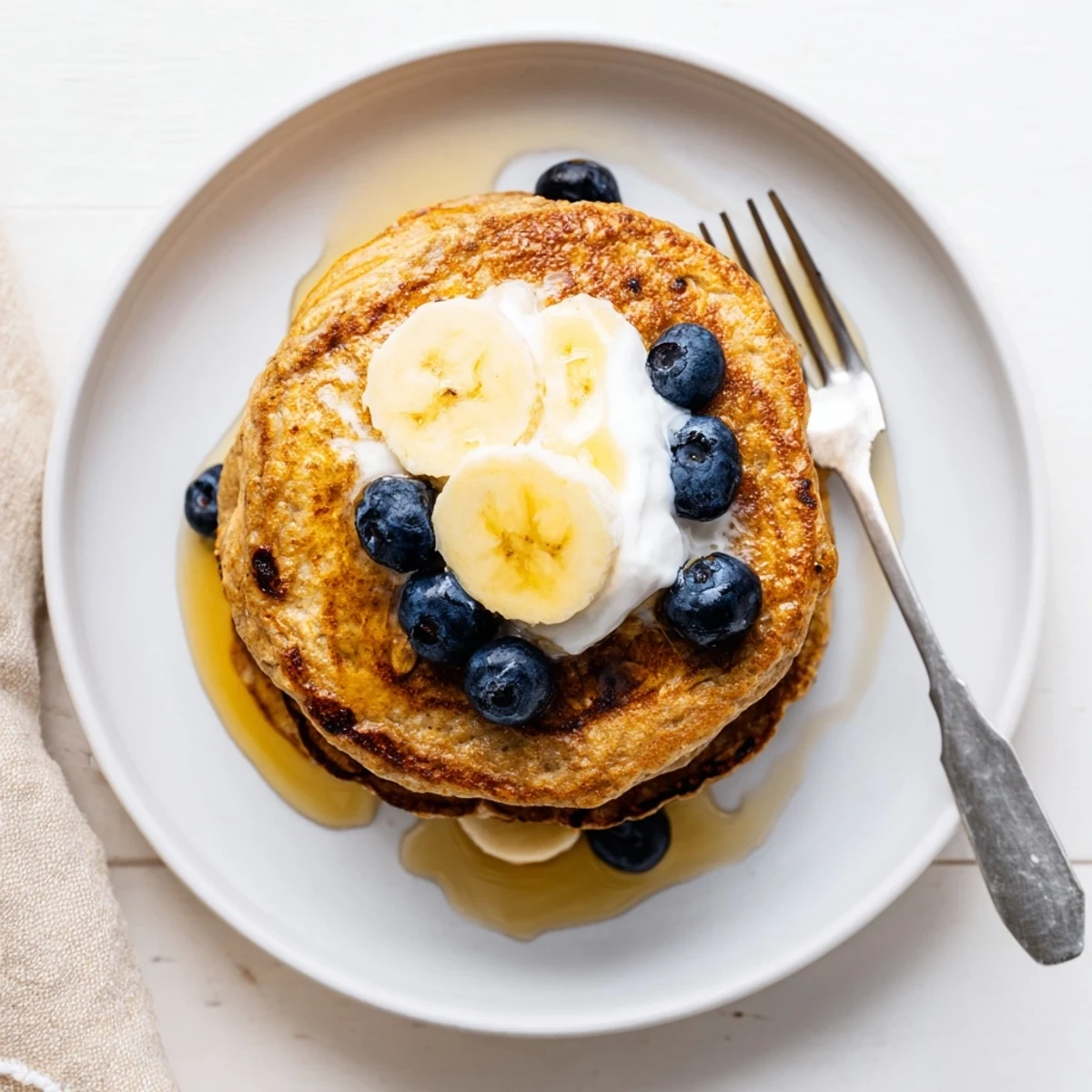 Stack of fluffy banana oatmeal pancakes topped with creamy Greek yogurt and fresh berries
