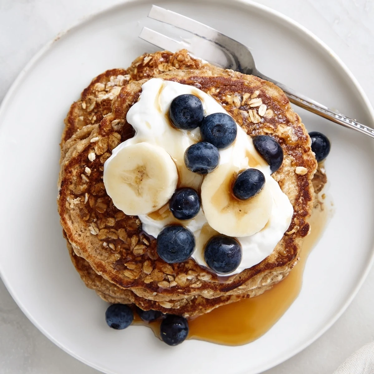 Healthy breakfast stack of banana oatmeal pancakes drizzled with maple and Greek yogurt
