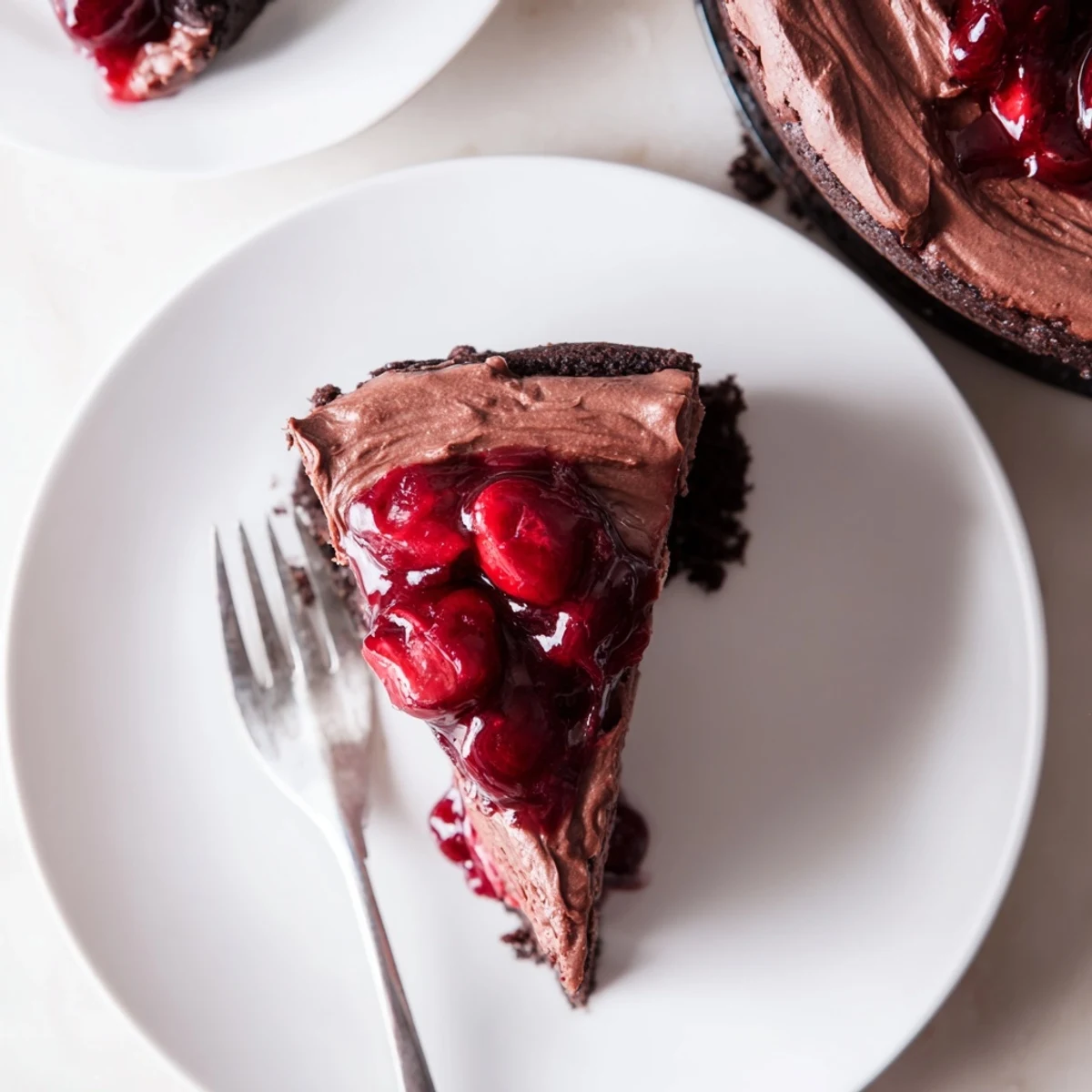 Creamy dark chocolate cherry cheesecake slice with glossy red cherry topping on white plate