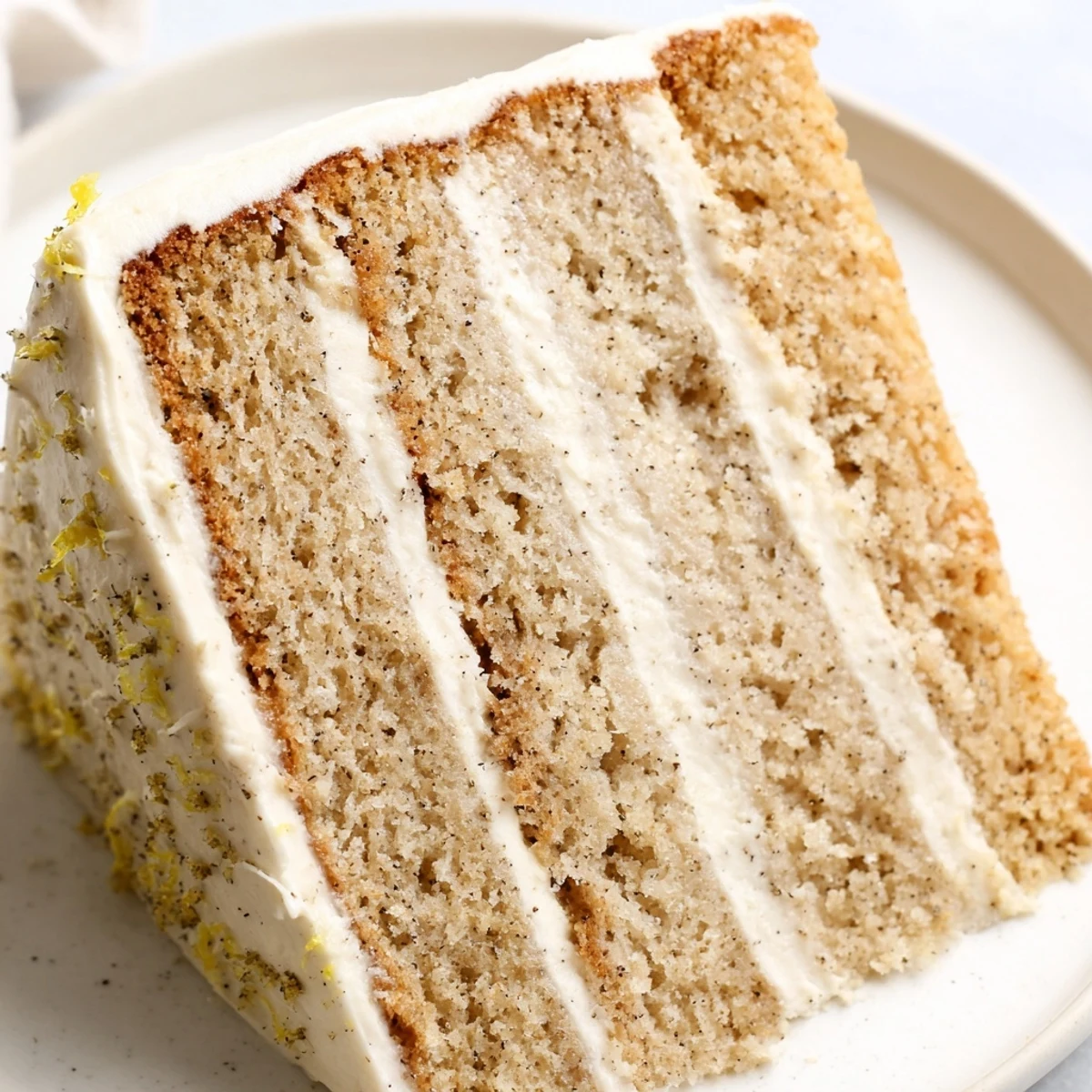 Triple-layer London Fog cake on serving plate featuring tea-steamed crumb and smooth vanilla frosting topped with bright citrus zest