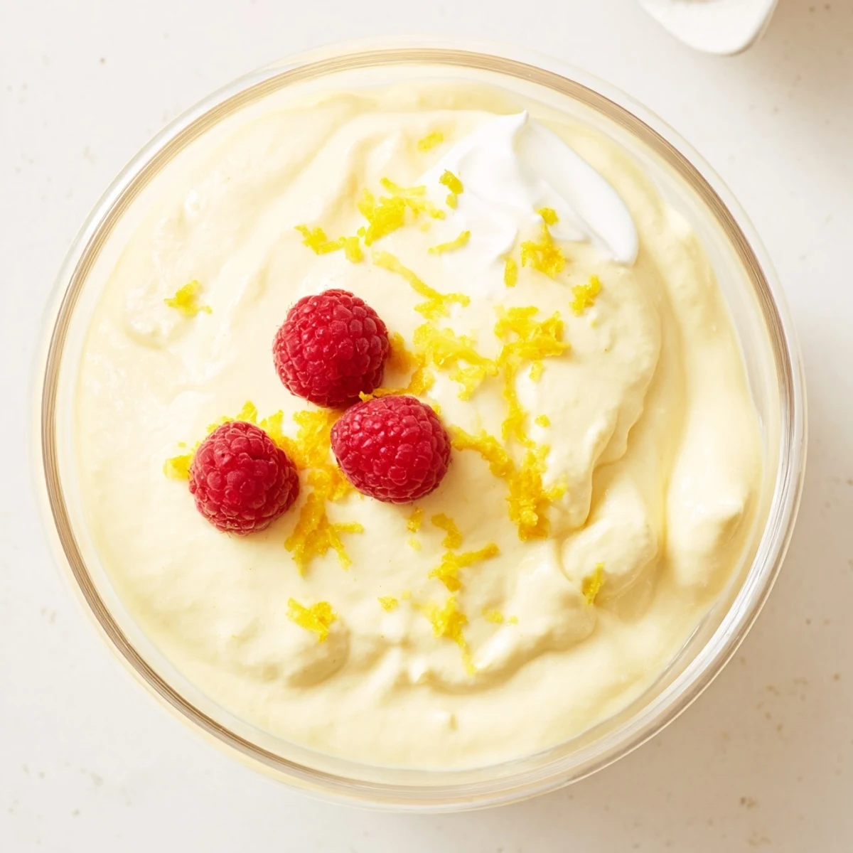 White serving bowl of smooth lemon cheesecake mousse with bright lemon twist garnish