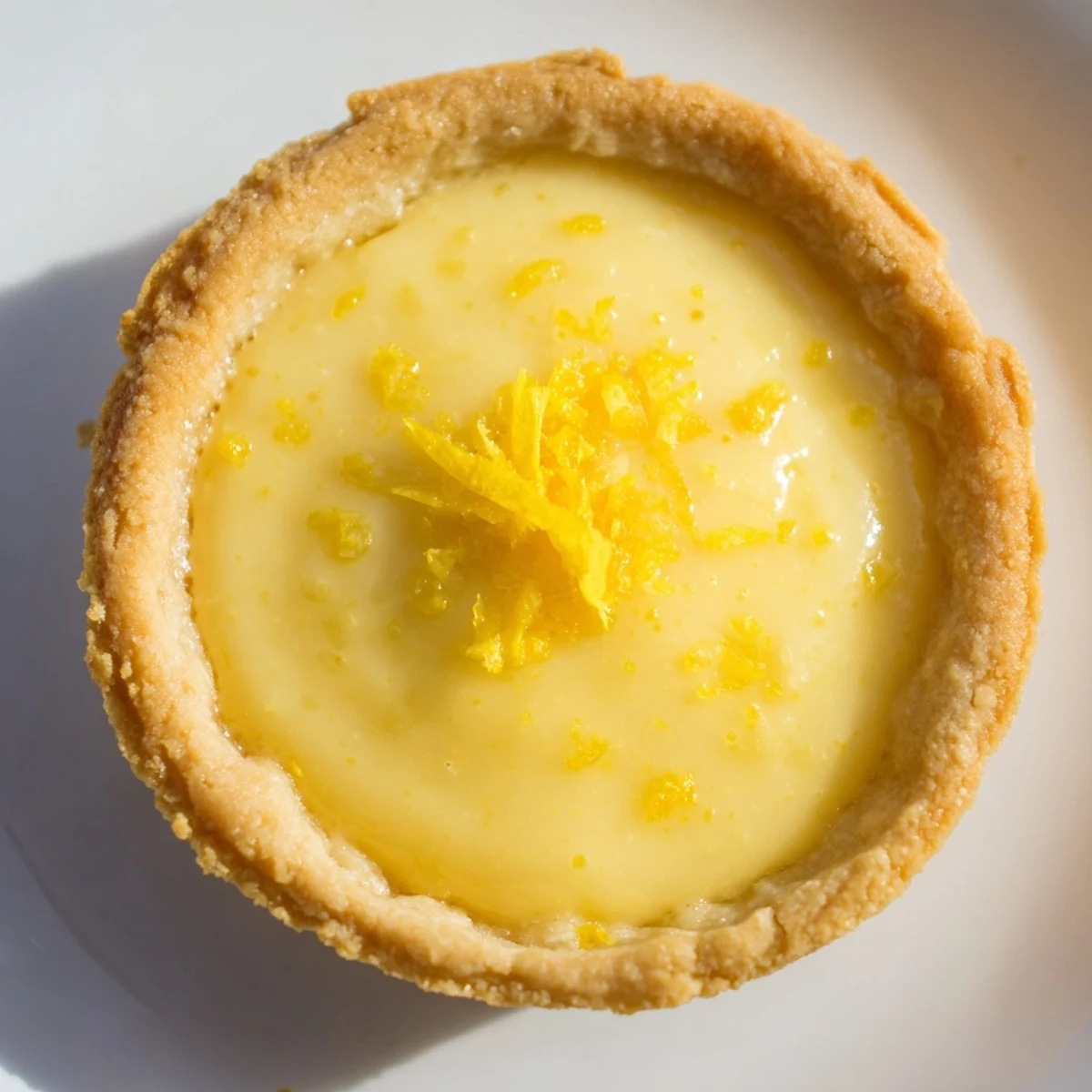 Golden mini vegan lemon tarts with smooth coconut cream filling in crisp pastry shells displayed on a white plate
