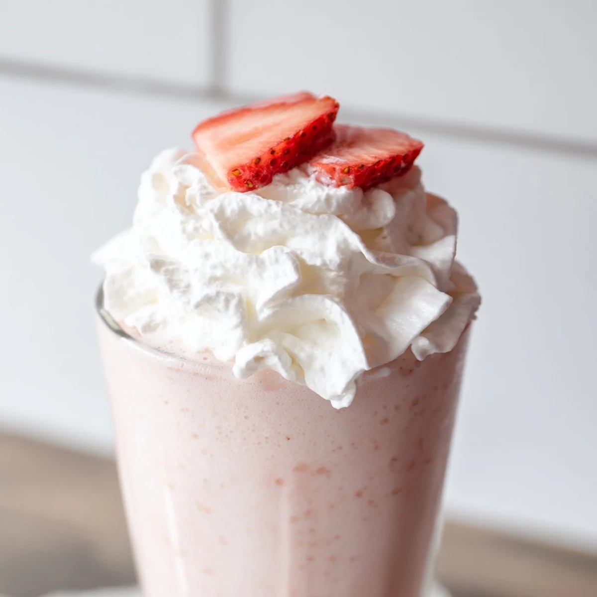 Tall glass of refreshing strawberry cream Frappuccino topped with fluffy whipped cream and fresh strawberry slices