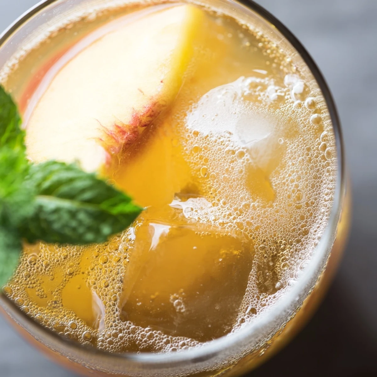 Golden Ginger Peach Sparkler drink topped with ice cubes and fresh peach wedge