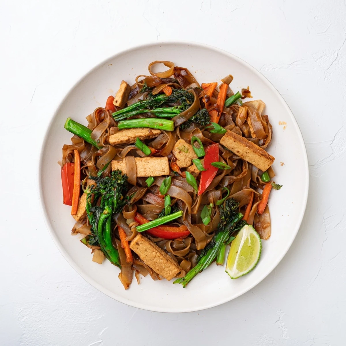 Vegan pad see ew featuring tender tofu strips, colorful vegetables, and glossy wide rice noodles coated in rich dark soy glaze