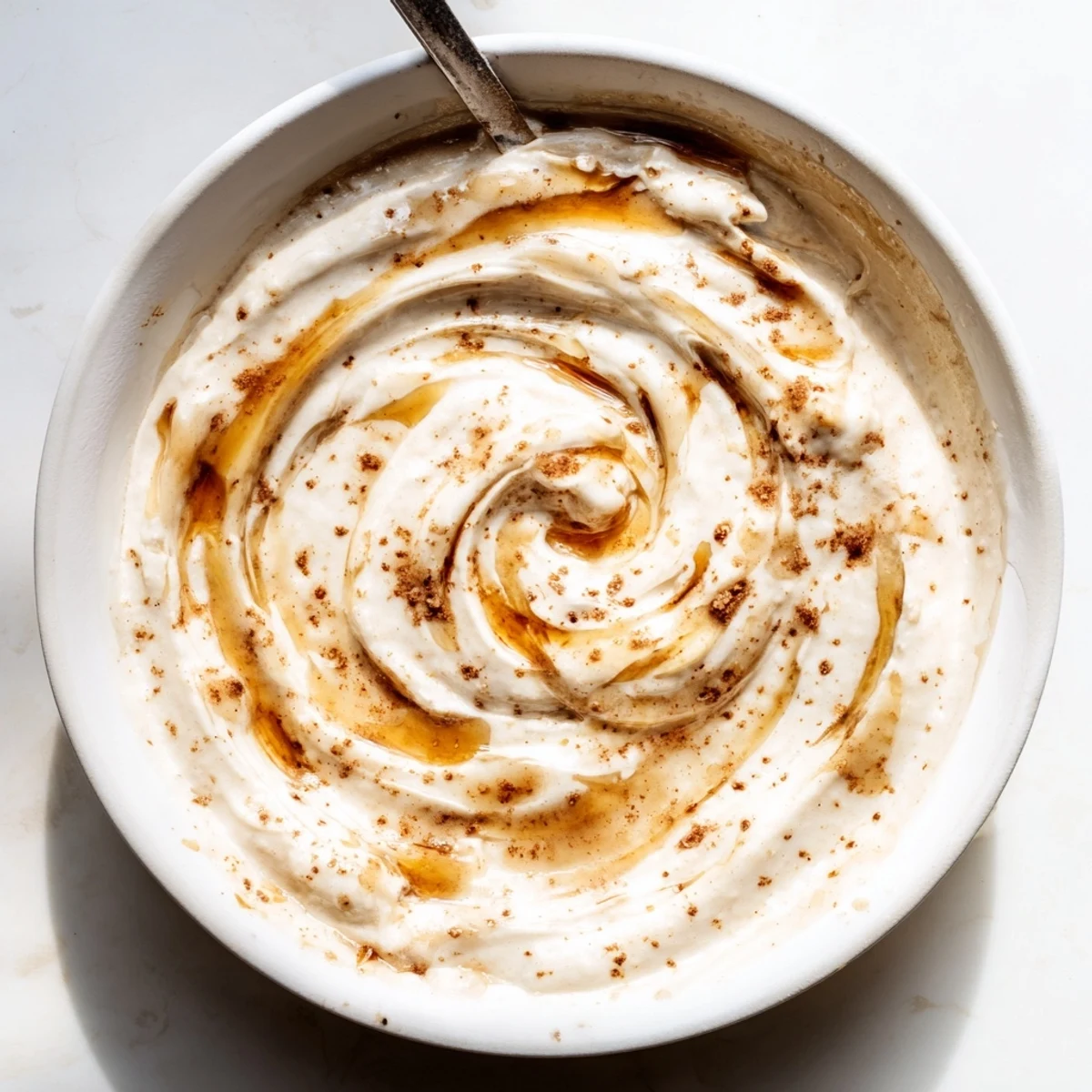 Healthy Greek yogurt cinnamon roll dip in a bowl with drizzled cinnamon topping and arranged pears grapes and banana slices
