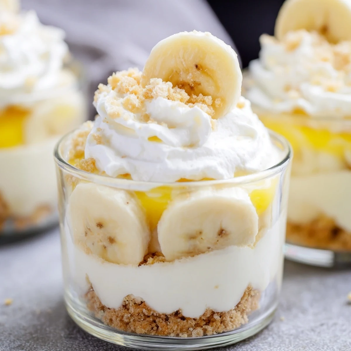 Creamy no bake banana pudding cheesecake cups with fresh banana slices and vanilla wafer crumbs on top