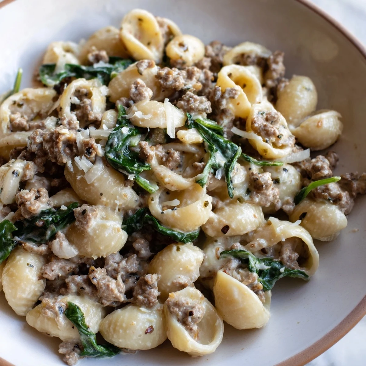 Creamy high protein beef pasta in a white bowl garnished with fresh Parmesan cheese