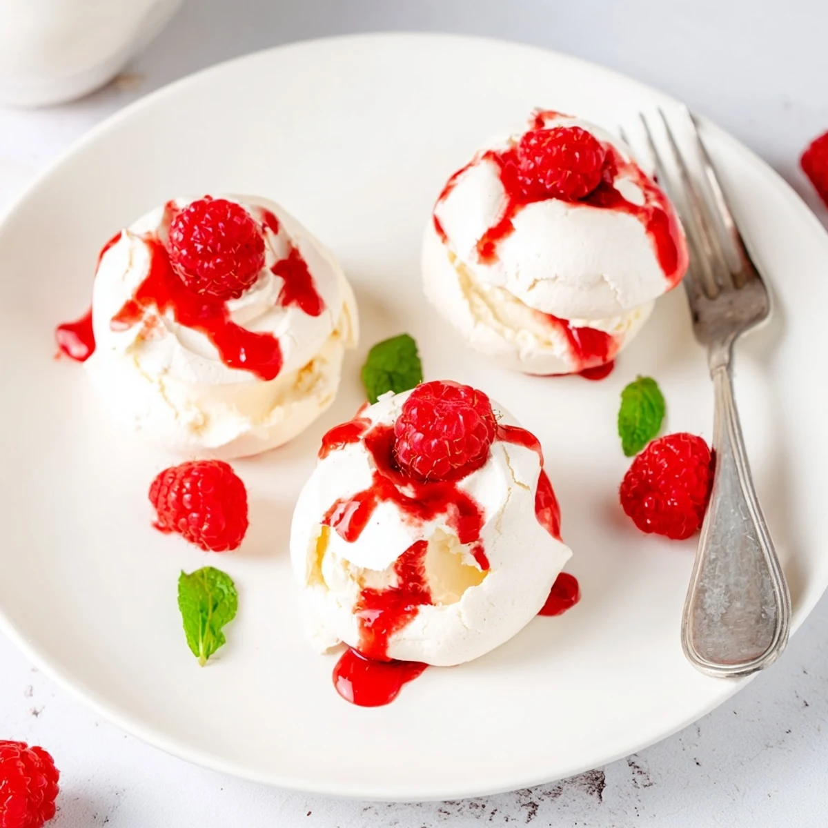 Bite-sized Pavlova bombs topped with fluffy whipped cream and tangy raspberry sauce