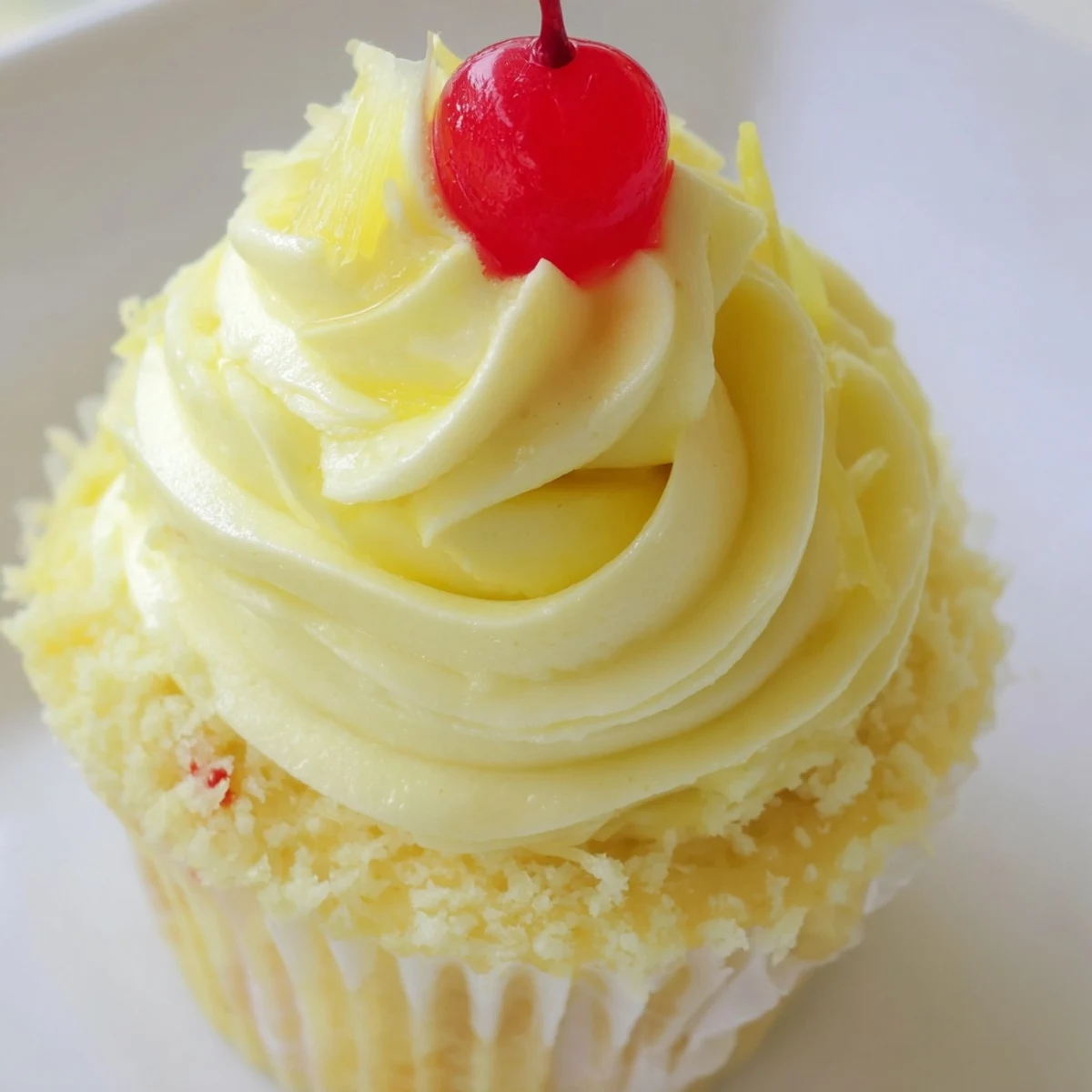 Moist pineapple Dole Whip Cupcakes topped with fluffy whipped frosting on a plate