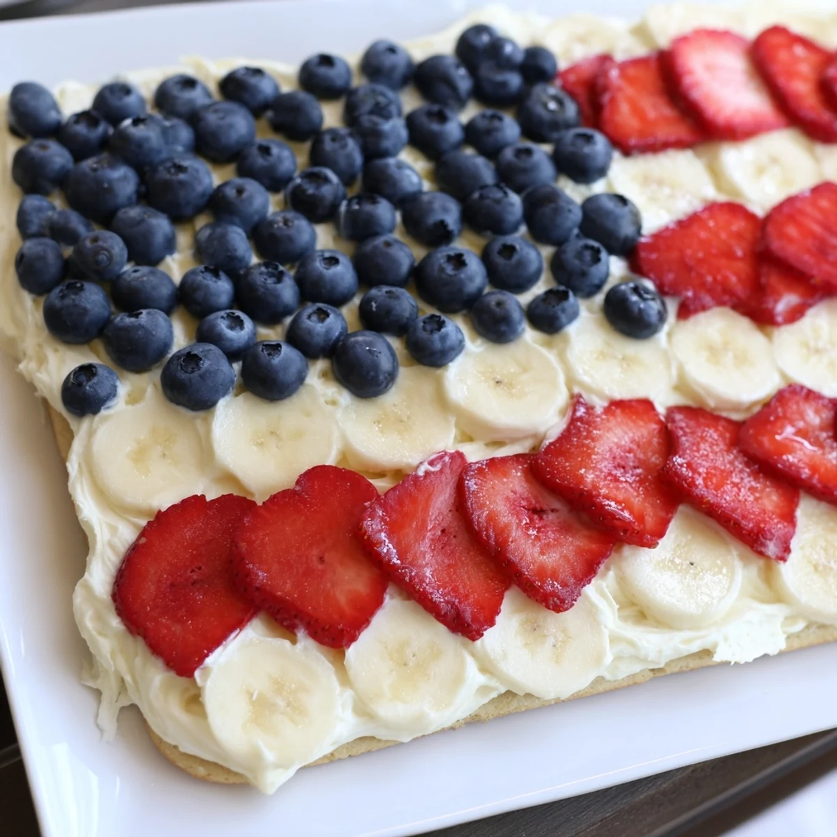 Sliced American Flag Fruit Pizza with creamy frosting, strawberries and banana stripes