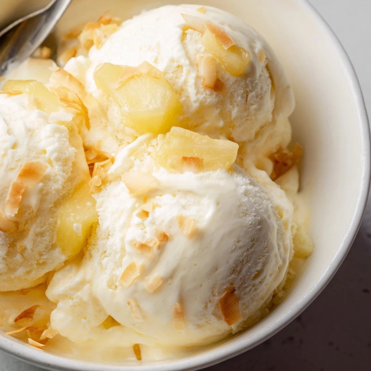 Homemade Creamy Pineapple Ice Cream spoonfuls melting slightly, bright tropical flavor