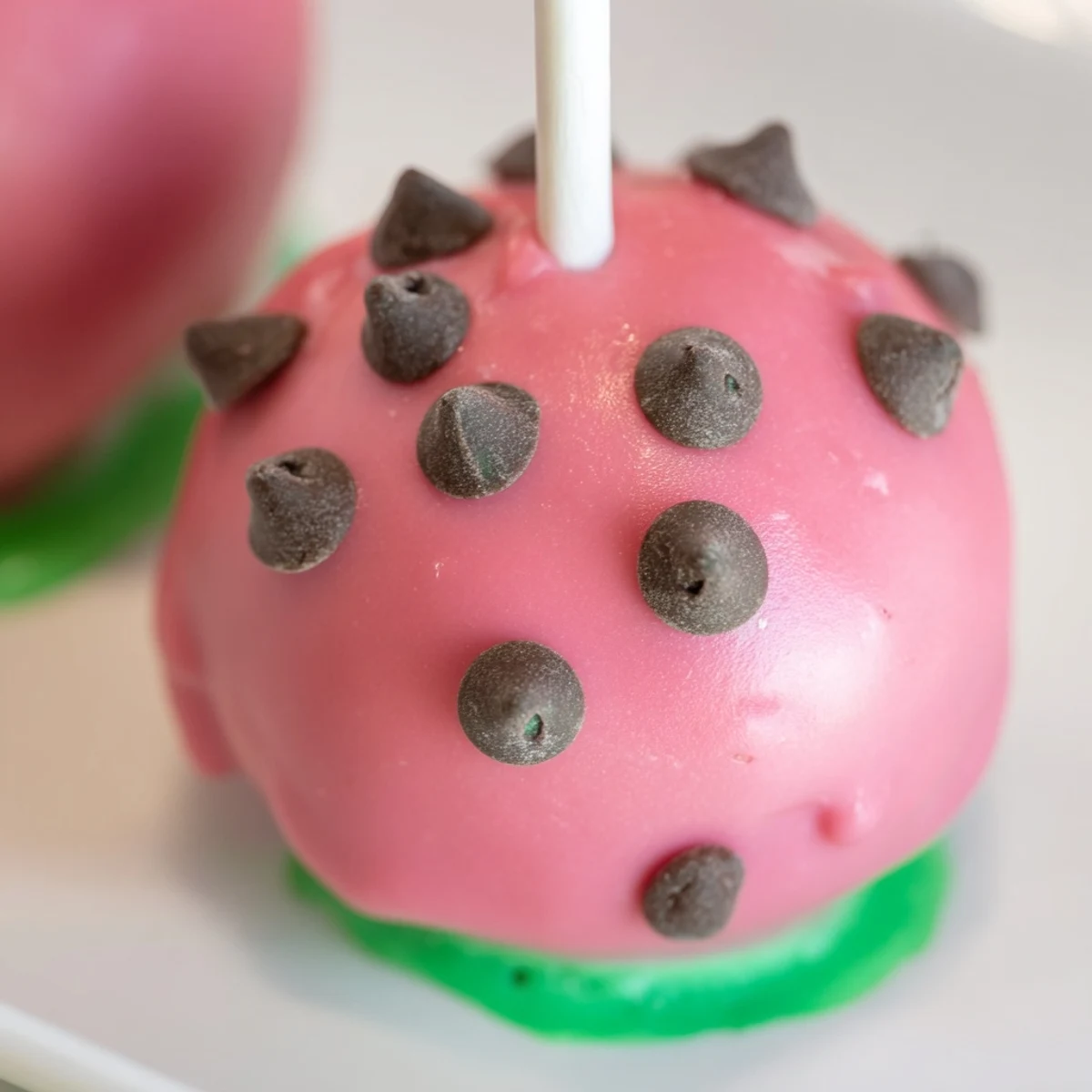Watermelon cake pops on lollipop sticks with pink coating, green rind, and mini chocolate chip seeds