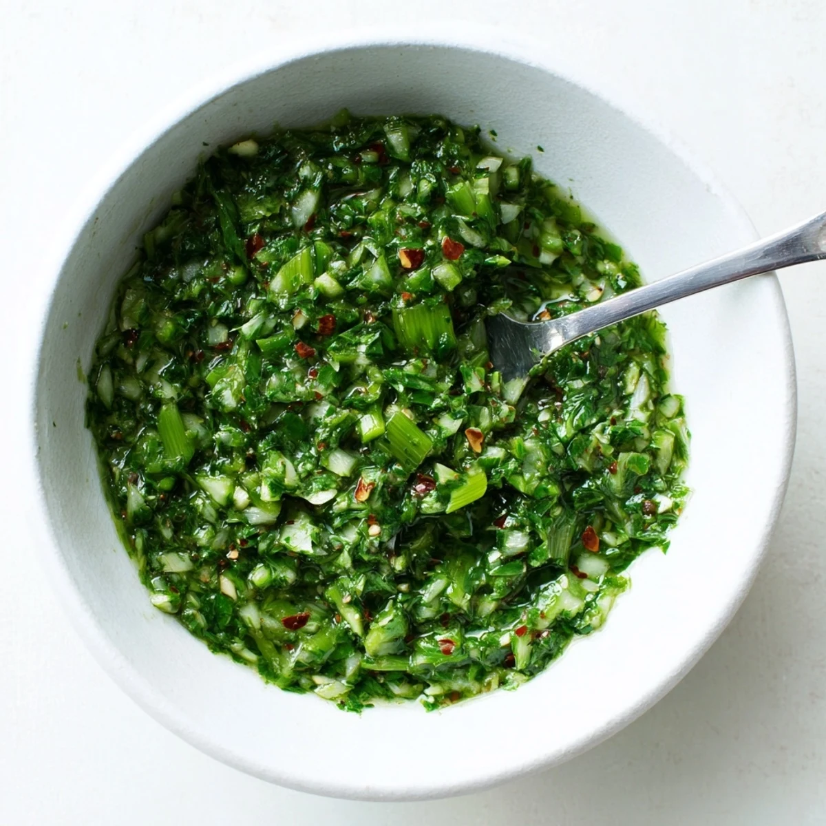 Spoonful of bright chimichurri sauce with garlic scapes atop grilled vegetables and meat
