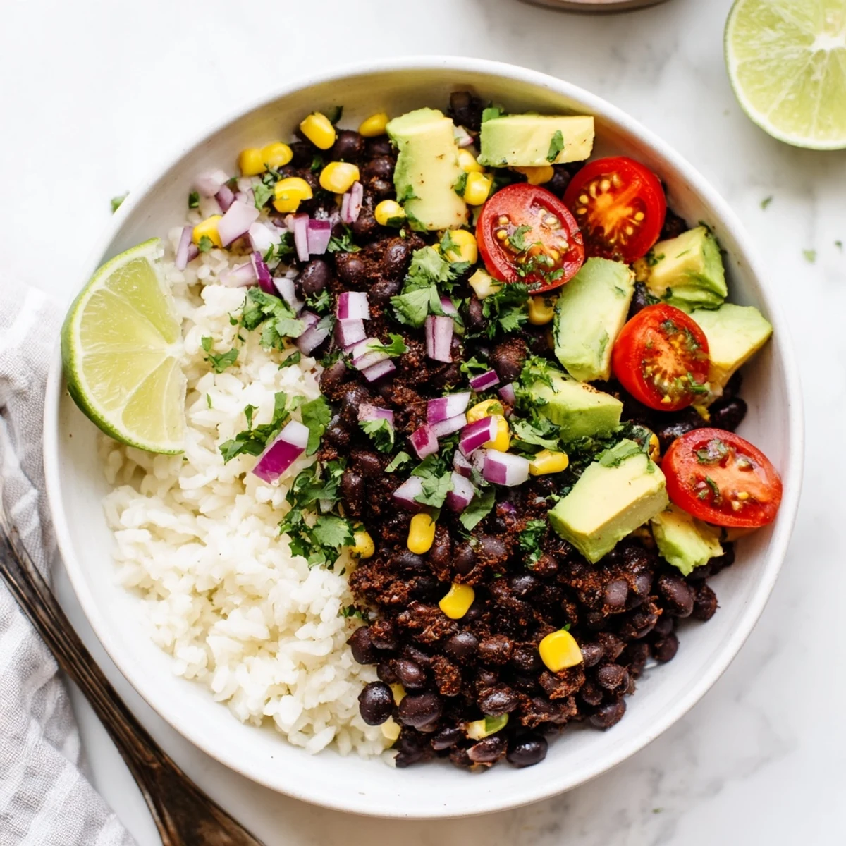 Hearty black bean and rice bowl garnished with sweet corn, lime wedges, and diced avocado