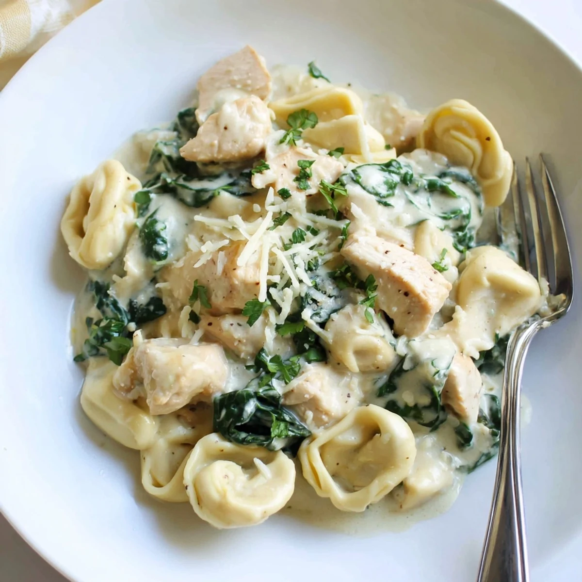 Creamy garlic chicken tortellini with spinach in a golden skillet topped with Parmesan