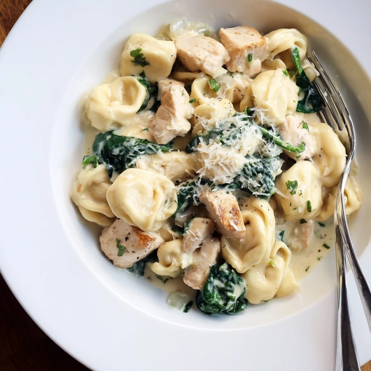 Steaming bowls of creamy garlic chicken tortellini with wilted spinach and fresh parsley