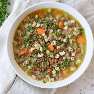 Steaming Lentil Noodle Soup in a rustic bowl, featuring tender lentils, carrots, celery, and egg noodles in a savory broth.