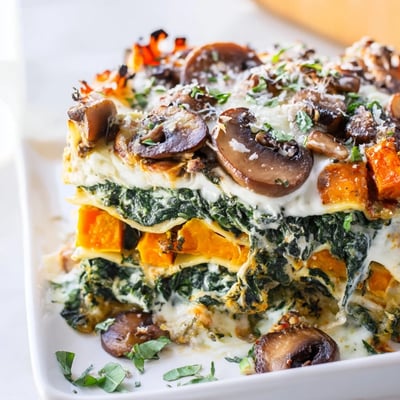 A hearty slice of Butternut Squash, Spinach & Mushroom Lasagna reveals roasted squash and spinach layers.