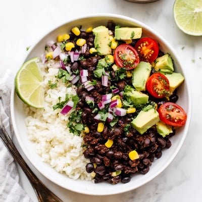 Hearty black bean and rice bowl garnished with sweet corn, lime wedges, and diced avocado