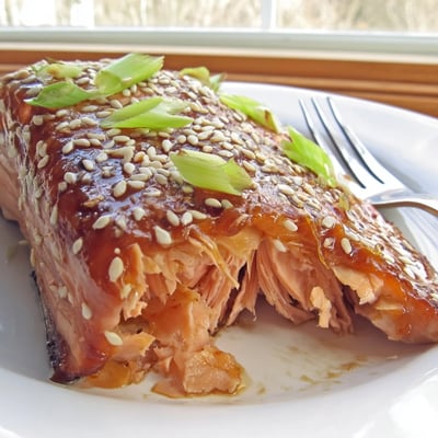 Golden baked Asian salmon garnished with green onions on a white dinner plate